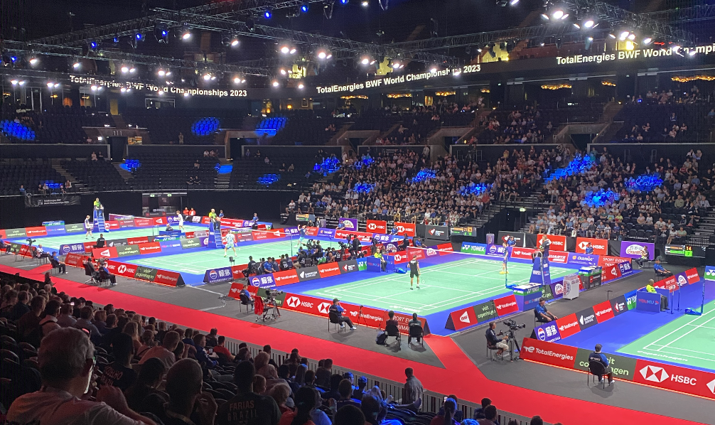 Crowded badminton stadium with 4 green badminton courts